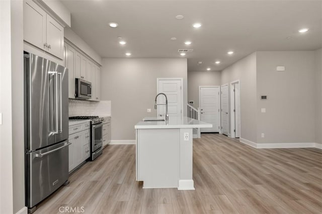 kitchen featuring stainless steel appliances, a sink, light countertops, light wood-type flooring, and a center island with sink