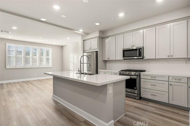 kitchen featuring a kitchen island with sink, a sink, visible vents, light countertops, and appliances with stainless steel finishes