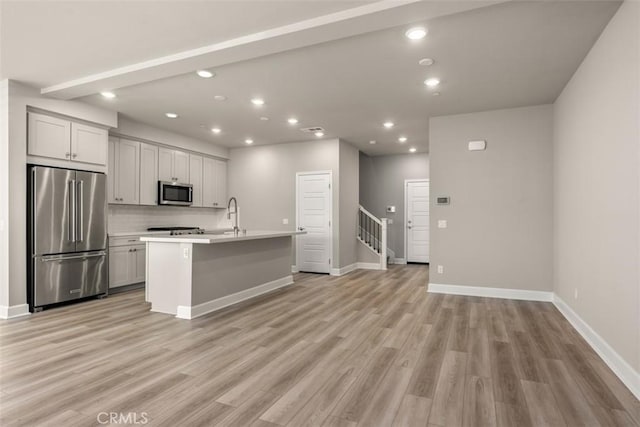 kitchen featuring light wood finished floors, light countertops, appliances with stainless steel finishes, and a center island with sink