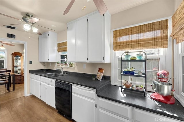 kitchen with black dishwasher, dark countertops, a sink, and white cabinetry