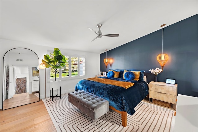 bedroom featuring wood finished floors, visible vents, baseboards, ceiling fan, and an accent wall