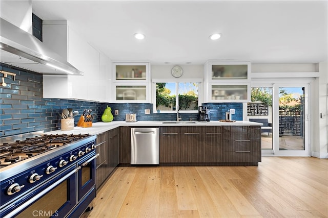 kitchen with light countertops, stainless steel appliances, white cabinetry, wall chimney exhaust hood, and a sink