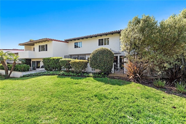 rear view of property with stucco siding, a tiled roof, a yard, and fence