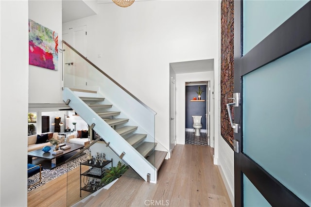 staircase featuring baseboards, wood finished floors, and a towering ceiling