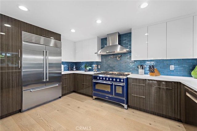 kitchen with wall chimney range hood, high quality appliances, light countertops, white cabinetry, and modern cabinets