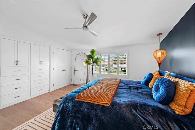 bedroom featuring a ceiling fan, vaulted ceiling, light wood-style floors, and multiple closets