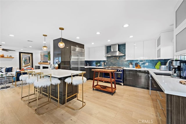 kitchen with light wood-type flooring, modern cabinets, wall chimney range hood, light countertops, and high end appliances