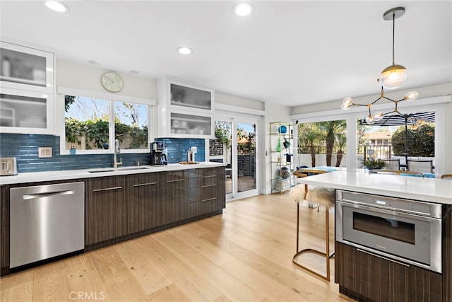 kitchen with a sink, appliances with stainless steel finishes, light wood finished floors, dark brown cabinets, and light countertops