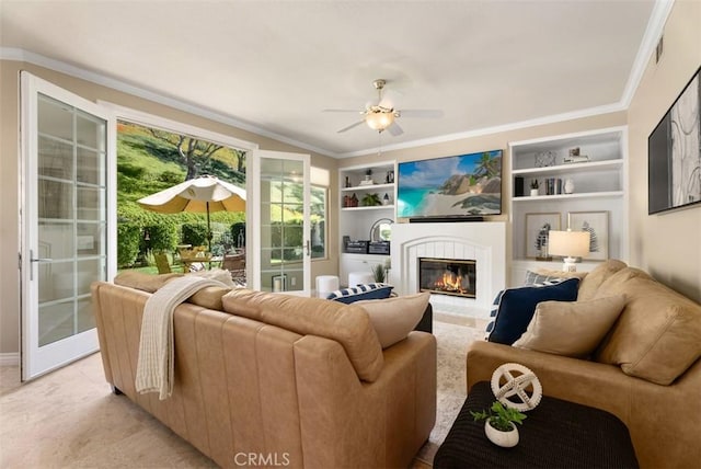 living room featuring ceiling fan, built in shelves, a glass covered fireplace, and crown molding