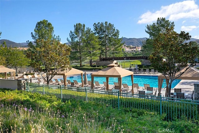 community pool featuring a patio area, a mountain view, and fence