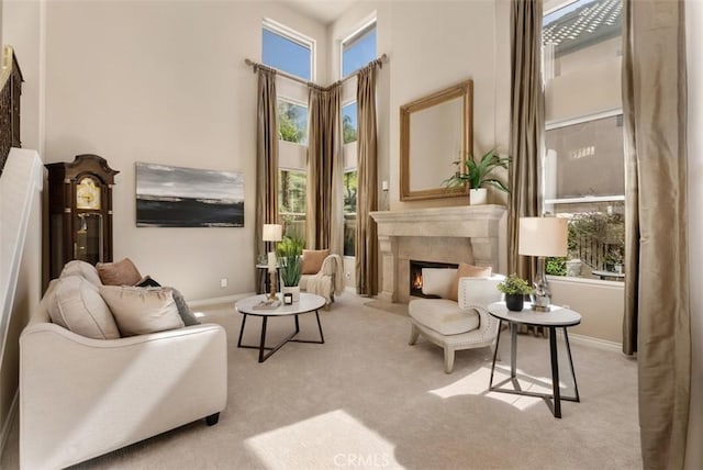 sitting room featuring a high ceiling, a warm lit fireplace, carpet flooring, and baseboards