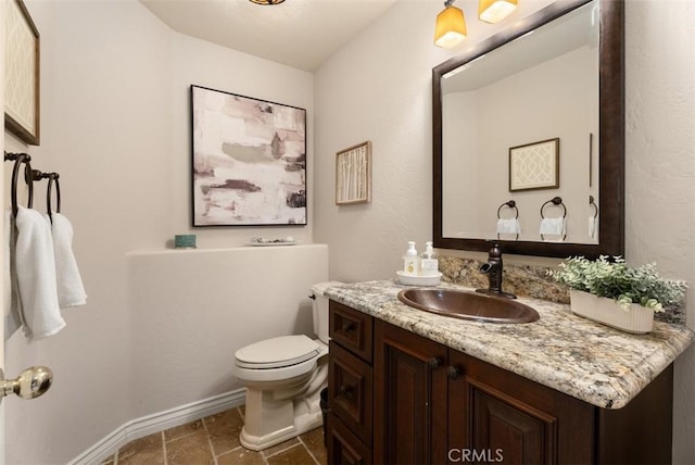 half bath featuring stone tile flooring, vanity, toilet, and baseboards