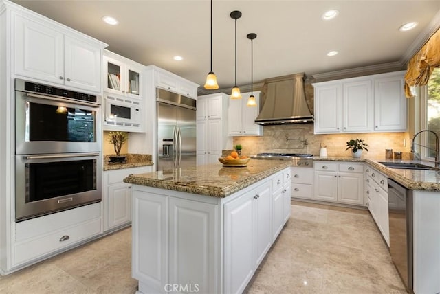 kitchen featuring wall chimney range hood, white cabinetry, a sink, and built in appliances