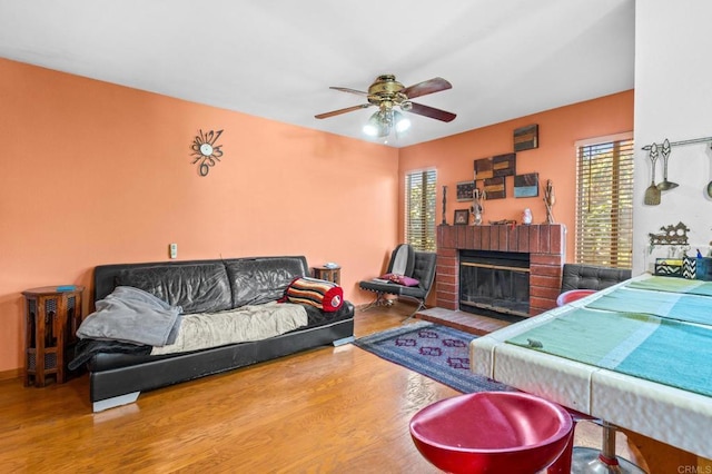 living room with ceiling fan, a brick fireplace, and wood finished floors