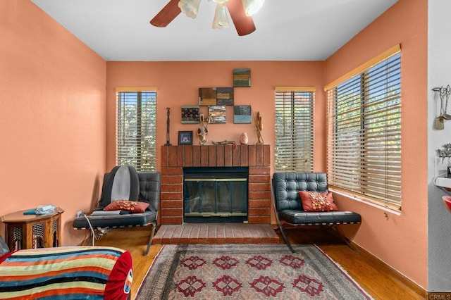 sitting room featuring a brick fireplace, ceiling fan, a wealth of natural light, and wood finished floors