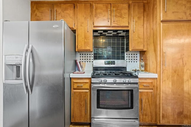 kitchen with brown cabinetry, tasteful backsplash, stainless steel appliances, and light countertops