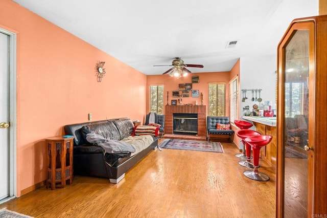 living area featuring a ceiling fan, light wood-type flooring, visible vents, and a fireplace