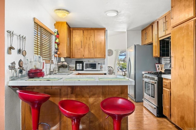 kitchen featuring a peninsula, brown cabinetry, stainless steel appliances, and a kitchen breakfast bar