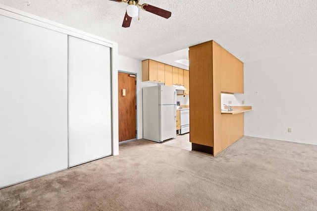 kitchen with light colored carpet, a ceiling fan, a textured ceiling, white appliances, and under cabinet range hood