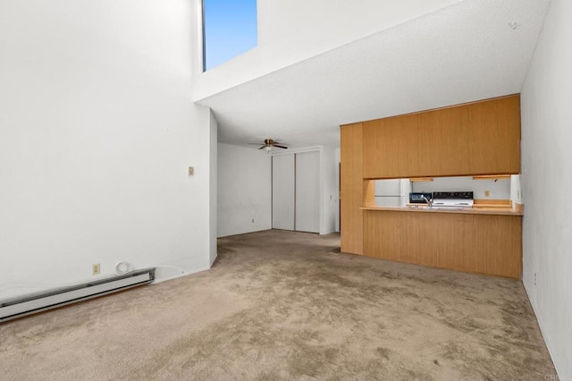 unfurnished living room with ceiling fan, a high ceiling, baseboard heating, and light colored carpet