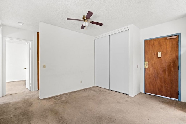 unfurnished bedroom featuring light carpet, ceiling fan, a textured ceiling, and a closet