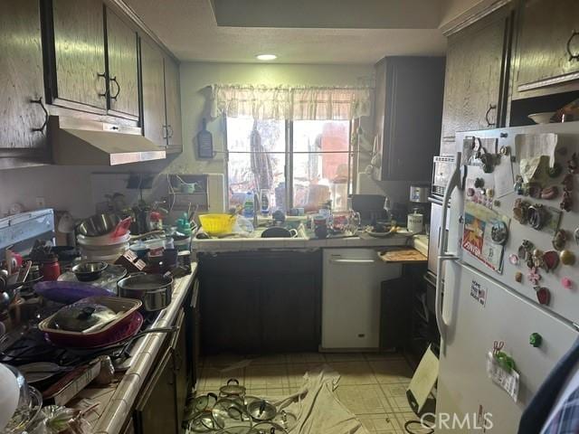 kitchen with light tile patterned floors, tile counters, dishwashing machine, freestanding refrigerator, and under cabinet range hood