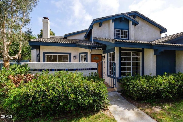 view of front of home featuring a tiled roof, a chimney, and stucco siding