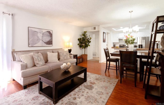 living area with a textured ceiling, wood finished floors, visible vents, and a notable chandelier