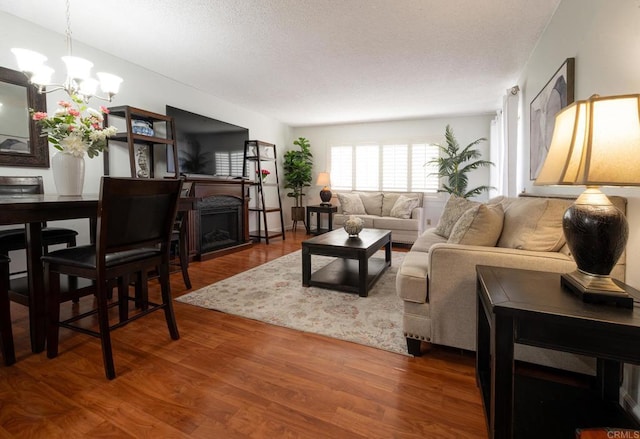 living area featuring a chandelier, a textured ceiling, wood finished floors, and a fireplace