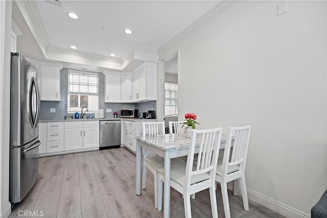 kitchen featuring decorative backsplash, appliances with stainless steel finishes, crown molding, white cabinetry, and a sink