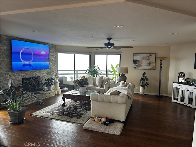 living room featuring dark wood-style floors, ceiling fan, baseboards, and a stone fireplace