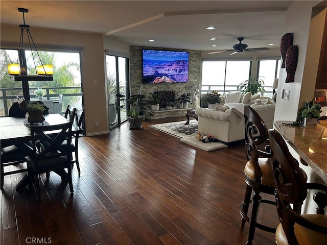 dining space with dark wood-style floors, a stone fireplace, plenty of natural light, and a ceiling fan