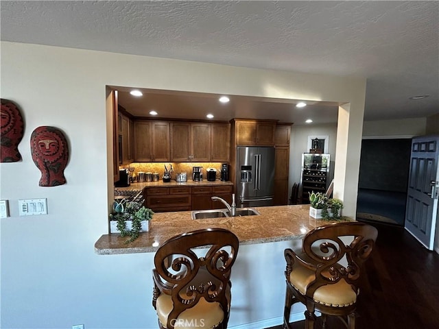 kitchen featuring light stone counters, a peninsula, high end refrigerator, a sink, and a kitchen breakfast bar