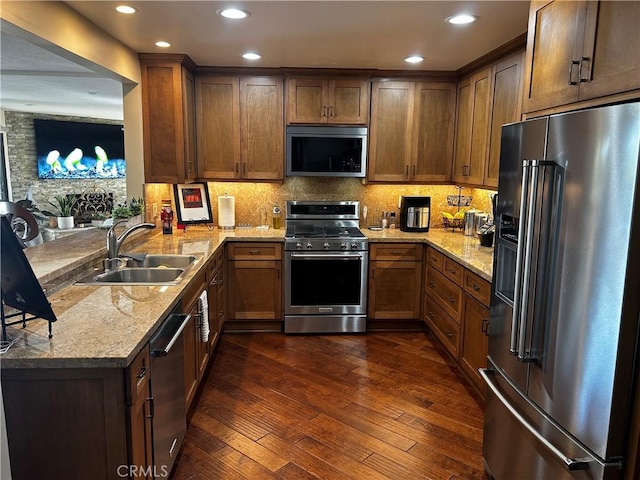 kitchen with light stone counters, dark wood finished floors, a peninsula, a sink, and appliances with stainless steel finishes