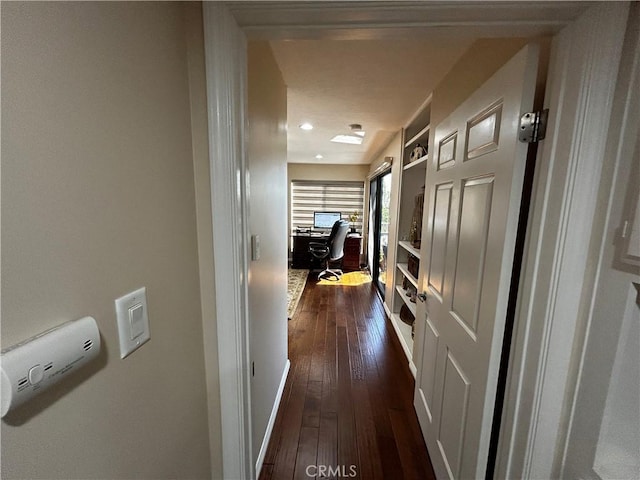 hallway featuring built in features, dark wood finished floors, and baseboards