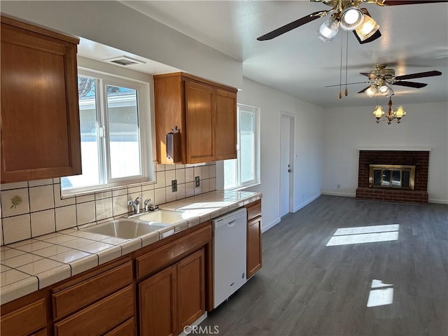 kitchen featuring a sink, a brick fireplace, tile counters, brown cabinets, and dishwasher