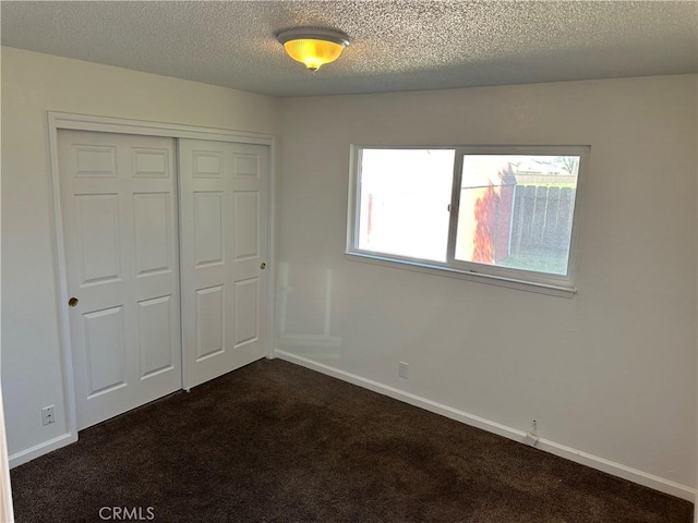 unfurnished bedroom with a textured ceiling, baseboards, dark colored carpet, and a closet