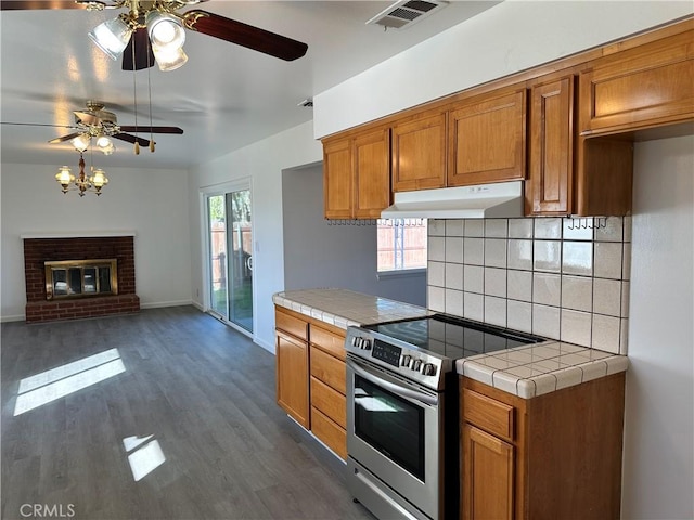 kitchen featuring tile countertops, under cabinet range hood, electric range, visible vents, and brown cabinets