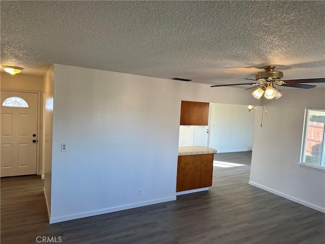 unfurnished room featuring baseboards, visible vents, dark wood finished floors, ceiling fan, and a textured ceiling