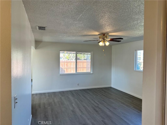 unfurnished room with plenty of natural light, dark wood finished floors, visible vents, and baseboards