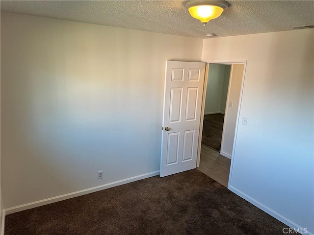 empty room with baseboards, visible vents, dark carpet, and a textured ceiling