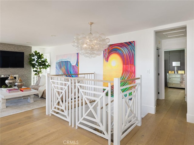 hall with baseboards, an upstairs landing, hardwood / wood-style flooring, and an inviting chandelier