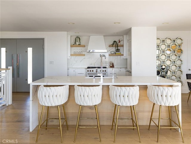 kitchen featuring a breakfast bar area, white cabinets, open shelves, stainless steel range, and custom range hood