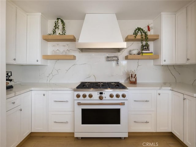 kitchen featuring light stone counters, white range, premium range hood, white cabinets, and open shelves