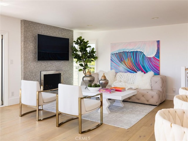 living room with a large fireplace, light wood-style flooring, and baseboards