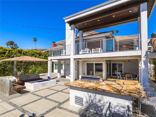 rear view of property featuring a patio area, a balcony, a bar, and an outdoor kitchen