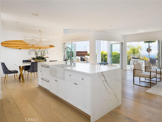 kitchen featuring pendant lighting, a center island with sink, light wood-style flooring, white cabinets, and a sink