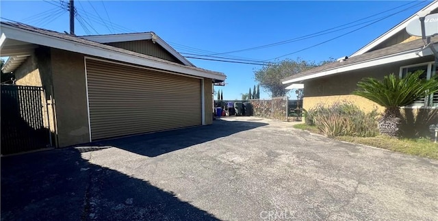 view of side of home with aphalt driveway, fence, and stucco siding