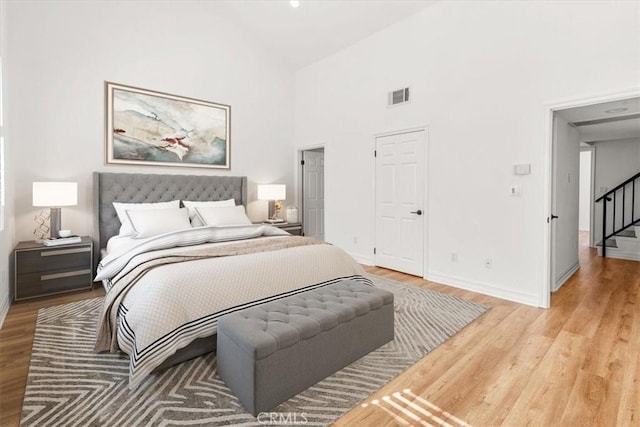 bedroom with high vaulted ceiling, visible vents, light wood-style flooring, and baseboards