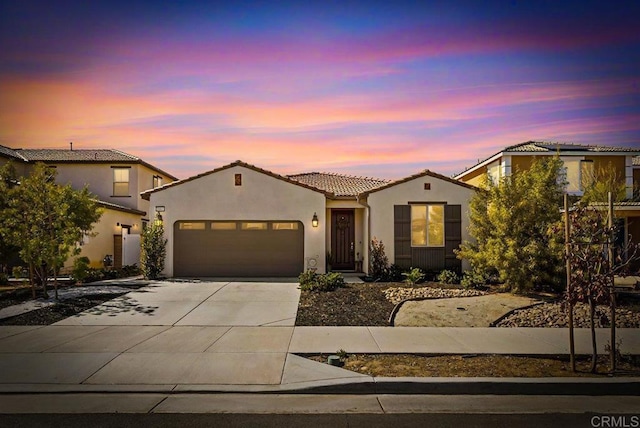 mediterranean / spanish-style house with a garage, driveway, a tile roof, and stucco siding